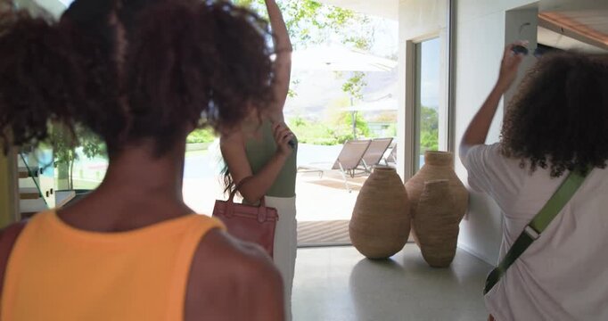 African American women arriving for vacation, opening pivot door using key fob, pulling suitcases