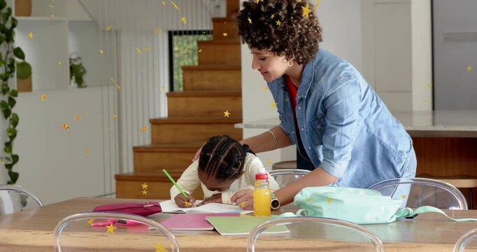 Adult woman leaning in and guiding school-aged girl at dining table, girl writing homework