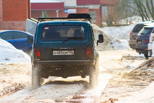 Lada Niva SUV splashes through muddy slush on a bright spring day in a Russian city, kicking up water droplets rear view: Russia - March 1, 2026