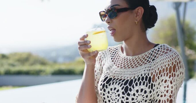 African American woman sitting poolside feeling thirsty, raising jar, sipping lemonade, copy space