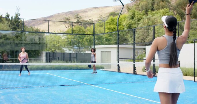 Female trio serving casually on blue court, right woman grey crop top swinging paddle, copy space