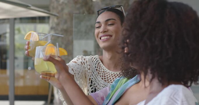 African American women toasting cocktails on patio after woman in white crochet top offering drinks