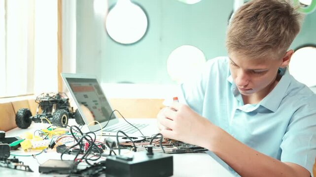 Caucasian boy fixing main board while study construction by using laptop analysis data. Young technician repairing and learning about using industrial structure at STEM technology class. Edification