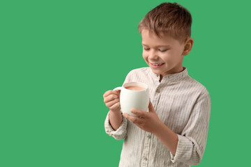 Cute little boy with cup of cocoa on green background