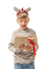 Naklejka premium Cute little boy in Christmas reindeer horns reading book on white background