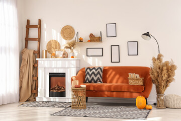 Naklejka premium Interior of living room with orange sofa, ladder, lamp, coffee table and autumn home decor on fireplace near white wall
