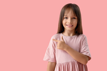 Fototapeta premium Portrait of cute little girl pointing at something on pink background