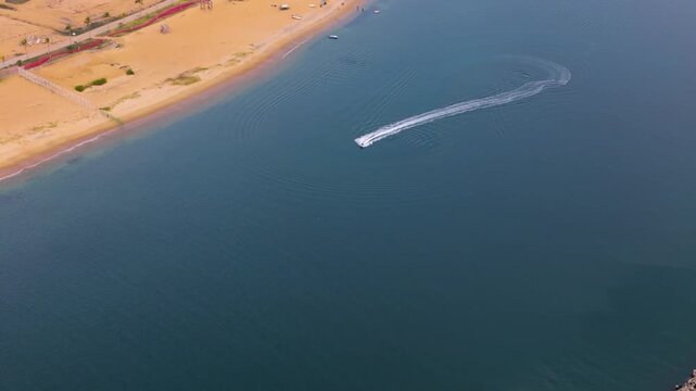 4K aerial view of a jet ski speeding and making sharp turns in clear blue ocean water near a sandy beach