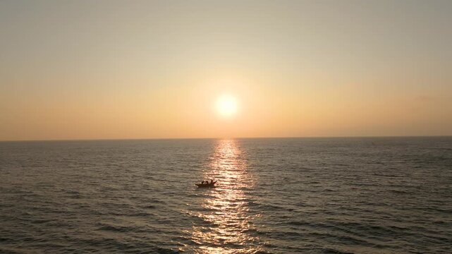 4K peaceful tropical evening showing a glowing sun setting behind coconut tree leaves with a fishing boat floating on the coast