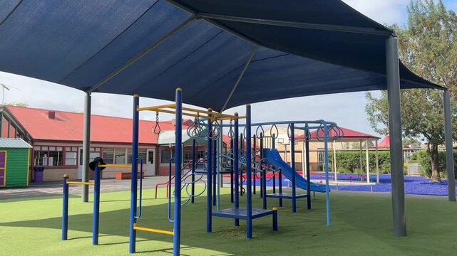Playground equipment under a large sun shade canopy at a public primary school in Australia. Outdoor school playground designed to provide sun protection for children in campus.