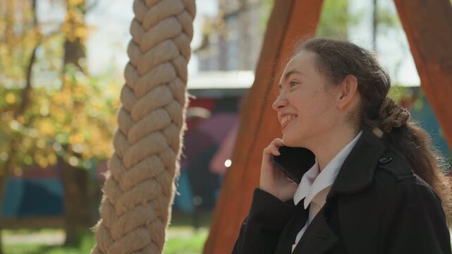 Joyful woman shares news. Smiling young woman announces marriage in park sunlight. Young woman with cheerful smile communicates exciting marriage update amidst autumn scenery and soft light