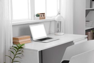 Fototapeta premium Blank laptop with books and lamp on desk in office