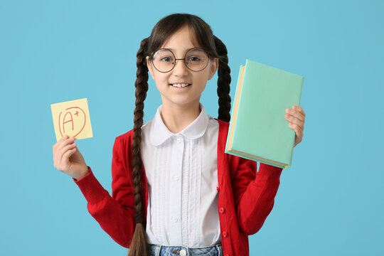 Happy schoolgirl holding book and sticky note with a-plus grade on blue background