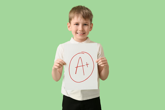 Happy schoolboy holding paper with a-plus grade on green background