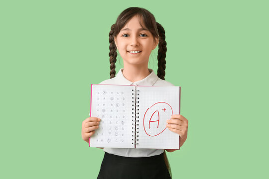 Happy schoolgirl holding notebook with good results of school test on green background