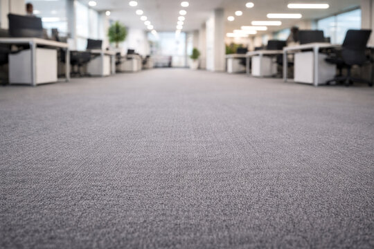 Low angle view of carpet floor in modern open office workspace with desks, computers and chairs blurred in background.
