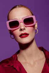 Close-up portrait of a fashionable woman wearing large pink sunglasses and red lipstick against...