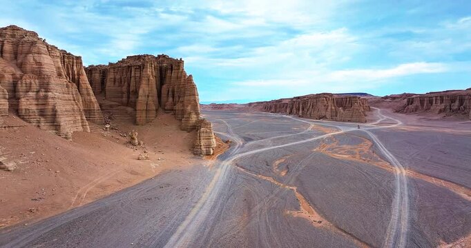 Aerial view of majestic Yardang landforms and winding dirt roads in the remote desert under a cloudy blue sky in Xinjiang, China.