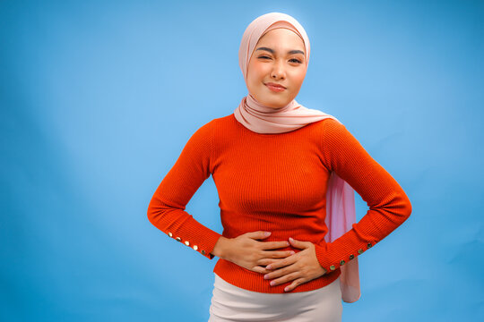 Sick Asian Muslim woman touching her stomach looking uncomfortable and experiencing abdominal pain.