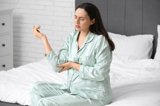 Pregnant young woman in pajamas suffering from pain in elbow on bed at home