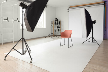 Interior of photo studio with professional equipment, chair and white backdrop