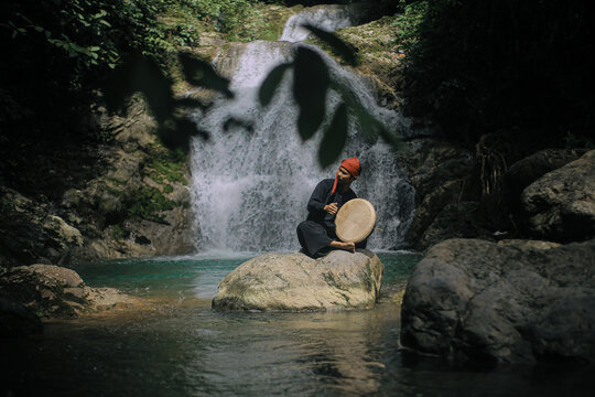 Acehnese Man Playing Traditional Rapai Drum at Waterfall &ndash; Cultural Music Performance in Tropical Nature, Indonesian Heritage and Travel Culture Concept