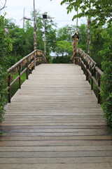 Fototapeta premium A peaceful view of a long wooden bridge stretching towards lush green trees, decorated with hanging wooden tags.