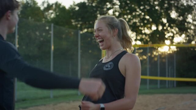 Student friends celebrate after scoring a point in outdoor volleyball at sunset. Happy teamwork moment on sand court with net and warm evening backlight