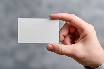 Fototapeta premium A person's hand professionally presents a clean, crisp, blank white rectangular card against a softly blurred, neutral grey background. The focus is on the empty space of the card, making it an ideal 