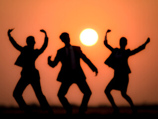 Fototapeta premium Joyful silhouettes dancing freely beneath a vivid setting sun.