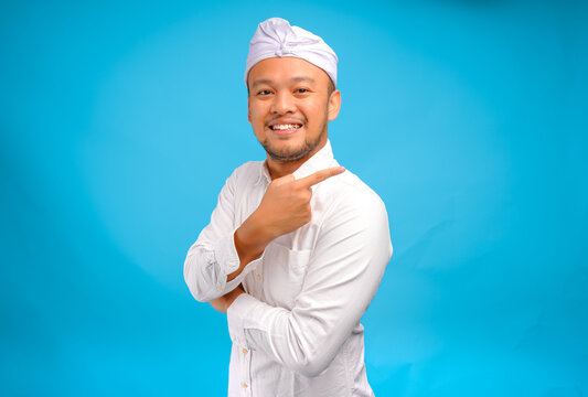 Happy Balinese man wearing Indonesian traditional udeng pointing to the copy space on behind him.