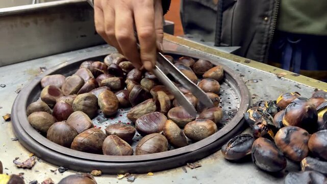 Close-up of a vendor using tongs to roast fresh chestnuts on a hot stove. Traditional winter street food in Istanbul, Turkey. Authentic local snack preparation at Galata Bridge, Bosphorus.