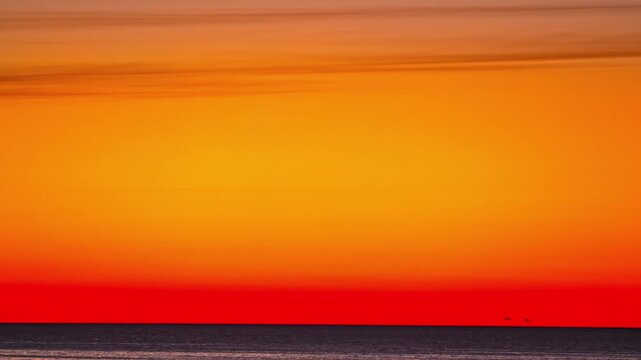 Timelapse of intense red and orange sunset over calm ocean horizon. Minimal sky composition with smooth color gradient and wide copy space for background design use.