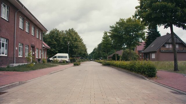 Beschreibung:
Locked off static shot of a quiet cobblestone village street in northern Germany. Brick houses, tree-lined road, overcast summer day, no people in sight.