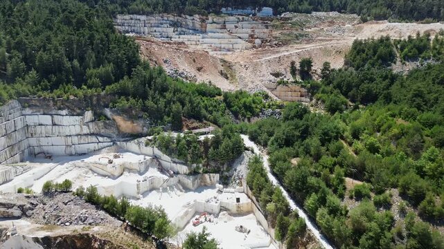 Aerial drone view of the Thassos marble quarry near Saliara, showcasing terraced extraction levels of world renowned pure white marble surrounded by forest landscape.
