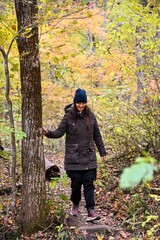Obraz premium Woman walking along forest trail during autumn solo hike. Calm wellness travel, mindful movement and peaceful rest in nature.