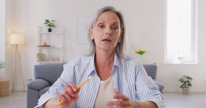 Confident senior elderly woman waving hand to webcam having webinar or video call sitting at home. Retired female person talking online. Retirement and communication technology concept. 4k video.
