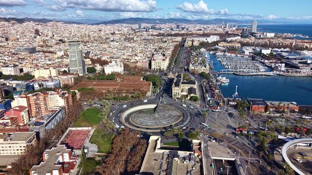 Aerial drone view of Port Vell area in Barcelona, the Columbus Monument, showing the Plaza de les Drassanes roundabout and the waterfront with the marina, Spain
