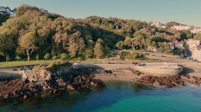 Havelet Bay Guernsey panning drone footage from bay to seawater bathing pools and beyond to St martin&rsquo;s Point with clear turquoise sea on calm sunny day in late afternoon with cloudless sky