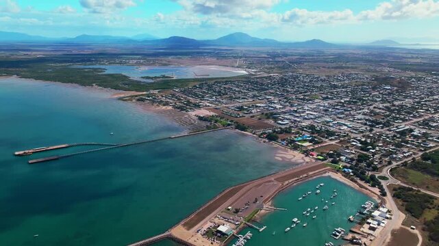 McCanes Bay Proserpine Bowen Jetty Coastal town Australia aerial drone landscape Horseshoe Bay Airlie Beach sunny blue sky marina boats cars harbor view Great Barrier Reef Whitsunday Region backwards
