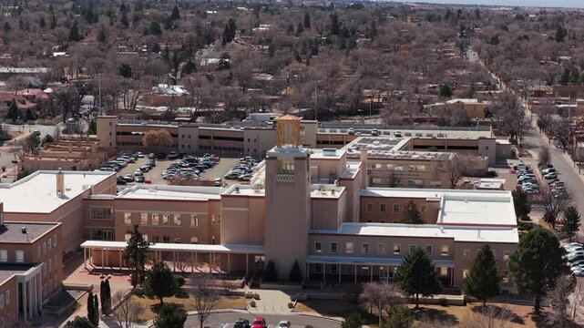 A smooth aerial orbit of the circular state capitol as two ravens fly across the frame. This 4K shot features the unique adobe architecture and local wildlife in Santa Fe.