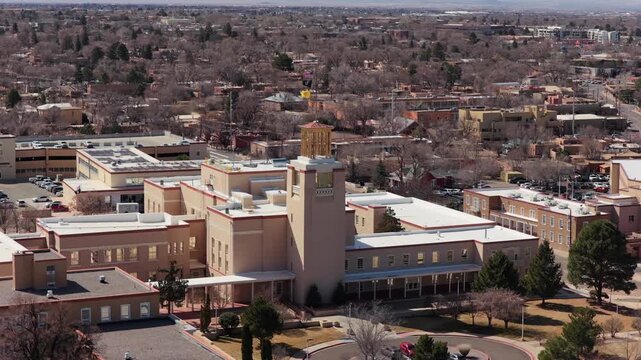 The camera moves in a steady arc around the iconic Roundhouse building in downtown Santa Fe. This 4K shot captures the heart of the state government district and the urban landscape.