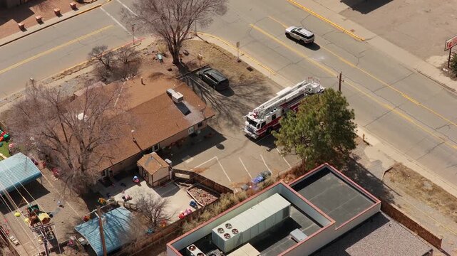 A high angle drone shot captures a red fire engine pulling into a parking lot. First responders begin to exit the vehicle in a professional community response scene in New Mexico.