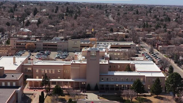 A smooth aerial orbit highlights the curved adobe-toned walls of the iconic state capitol. This 4K shot captures the distinct geometry of the central building.