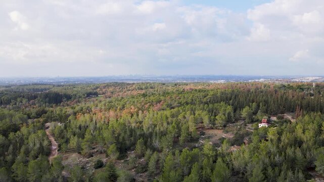 Drone shot panning and pulling back above Ben Shemen Forest, revealing dense woodland landscape under cloudy sky and expansive rural terrain.