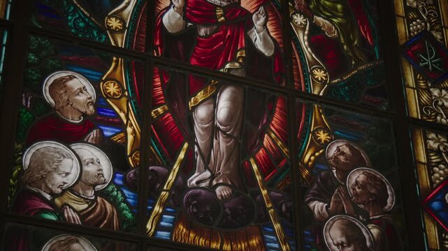 Vibrant stained glass window depicting Jesus Christ with raised hands in blessing, surrounded by saints in a richly detailed church interior.