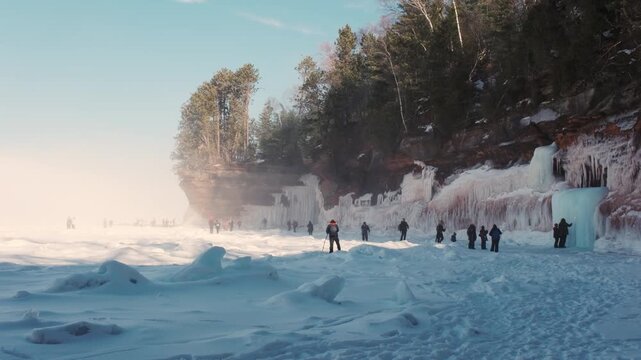 Hikers trek across the frozen Lake Superior shoreline beneath icy cliffs and icicles at the Apostle Islands ice caves.