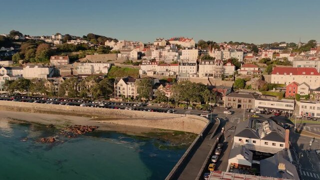 Havelet Bay St Peter Port Guernsey drone footage of seafront and beach with still calm clear sea and full view of esplanade in late afternoon sun with cloudless sky