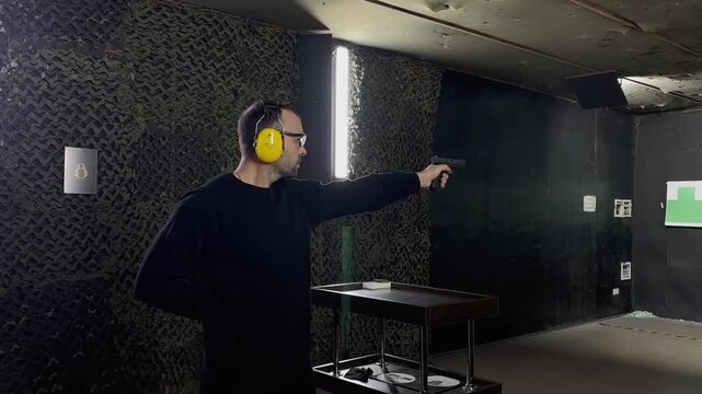Man points a pistol at a target at shooting range. Shooter aims and fires at a target during shooting practice.