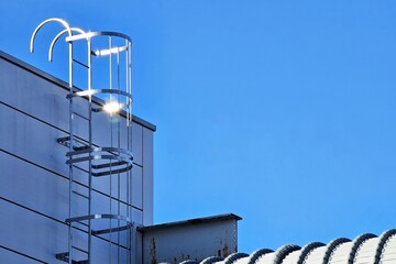 Minimal fixed aluminum ladder with a safety cage with blue sky background. © mesamong